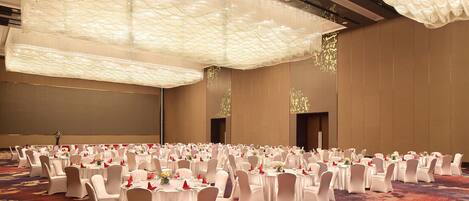 A banquet hall with round tables, white chairs, and a red carpet.