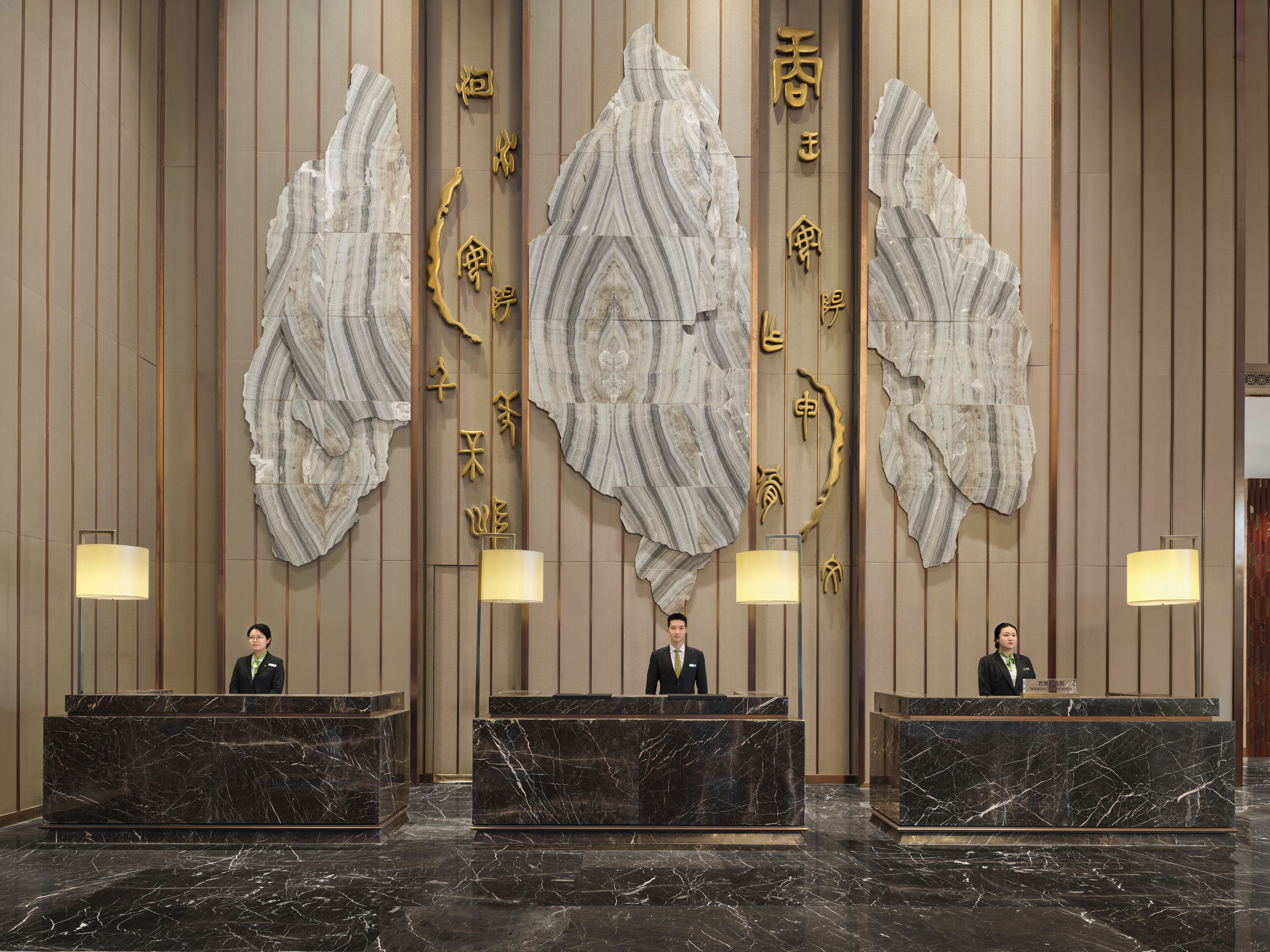 A hotel reception area with marble reception desks and large decorative wall panels.