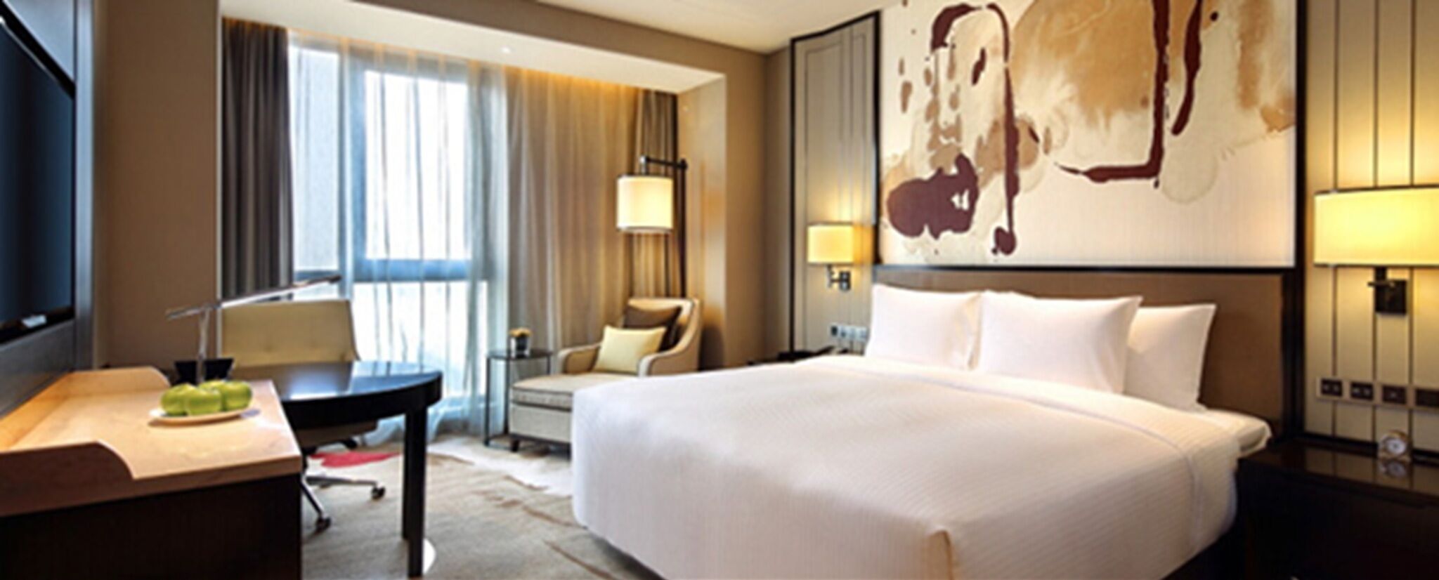 A hotel room with a bed, a desk, a chair, a lamp, and a painting on the wall.
