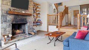 A cozy living room with a stone fireplace, wooden shelves, a blue sofa, and a wooden staircase. - Outpost: Spirit Dance 3110 - Summer Pool Access! (Jackson)