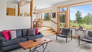 A modern living room with a grey sofa, wooden coffee table, and grey armchairs. There is a staircase leading to a balcony with a view of trees. - Outpost: Spirit Dance 3110 - Summer Pool Access! (Jackson)