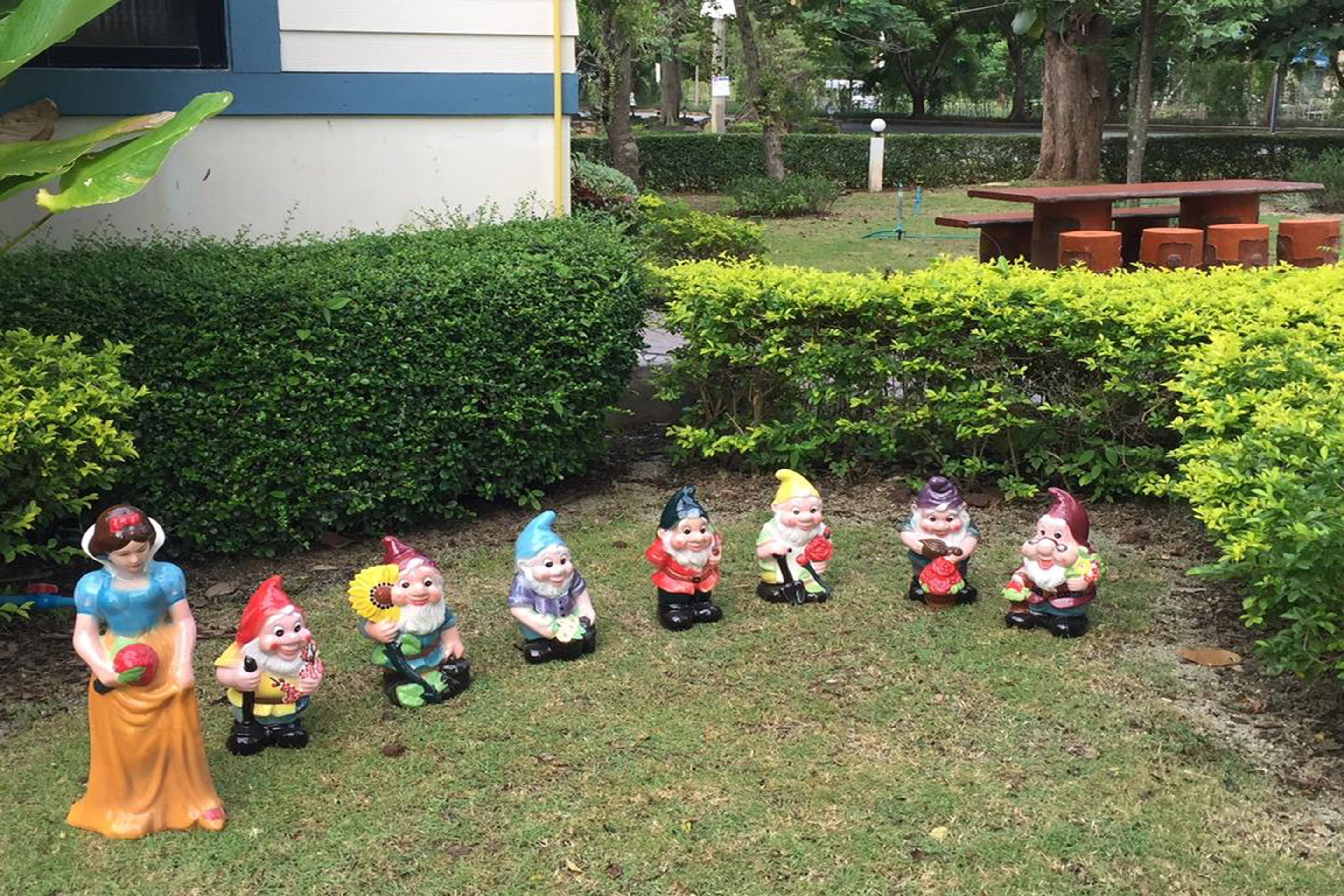 Un jardín con una hilera de estatuas de gnomos y una estatua de Blancanieves.