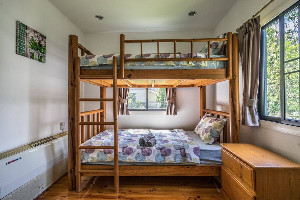 Une chambre avec un lit superposé, une échelle, une fenêtre avec des rideaux et un radiateur.