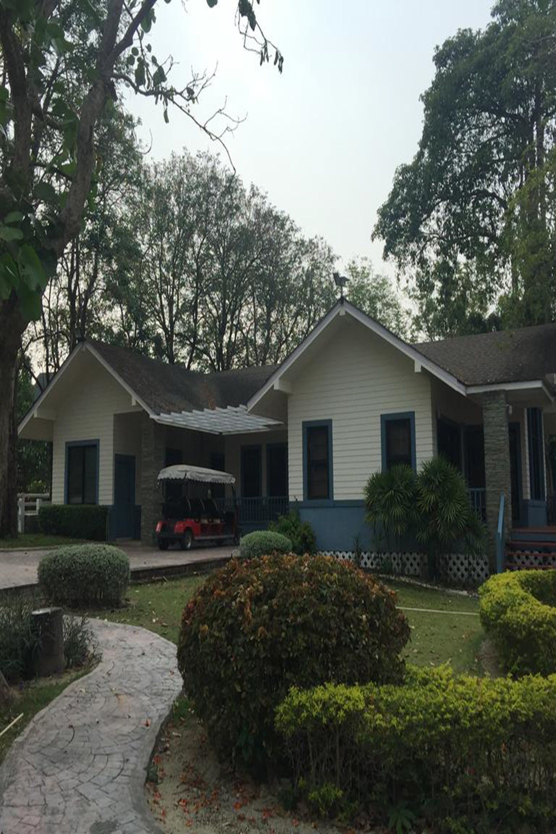 A two-story house with a covered porch, a driveway, and a small garden with bushes and a tree.