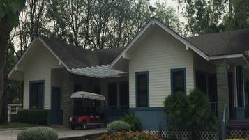 A two-story house with a covered porch, a driveway, and a small garden with bushes and a tree.