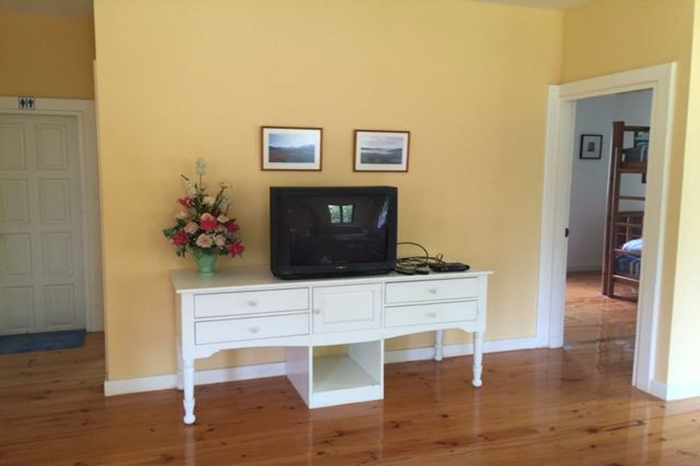 A room with a white dresser, a television on top, and two framed pictures on the wall.