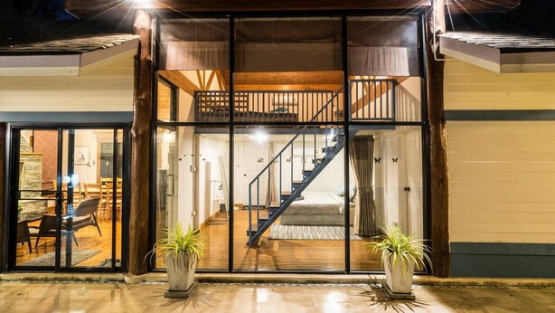 Ein modernes Haus mit Glastür, einer Treppe, die zu einem Schlafzimmerboden führt, und zwei Kübelpflanzen davor.
