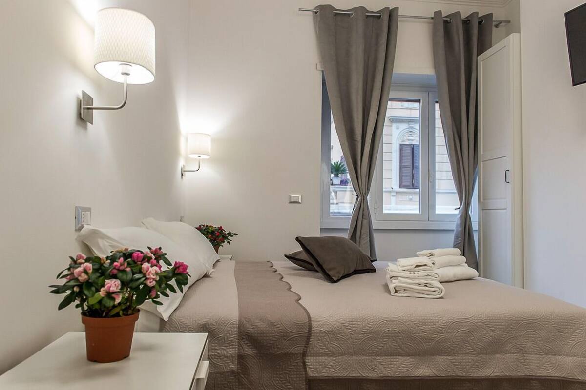 A neatly arranged bedroom with a bed, a bedside table with a potted plant, a lamp, and a window with curtains.