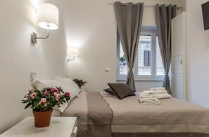 Ein ordentlich eingerichtetes Schlafzimmer mit einem Bett, einem Nachttisch mit Topfpflanze, einer Lampe und einem Fenster mit Vorhängen.