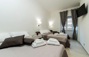 Habitación de hotel con dos camas, un televisor montado en la pared y una ventana con cortinas.