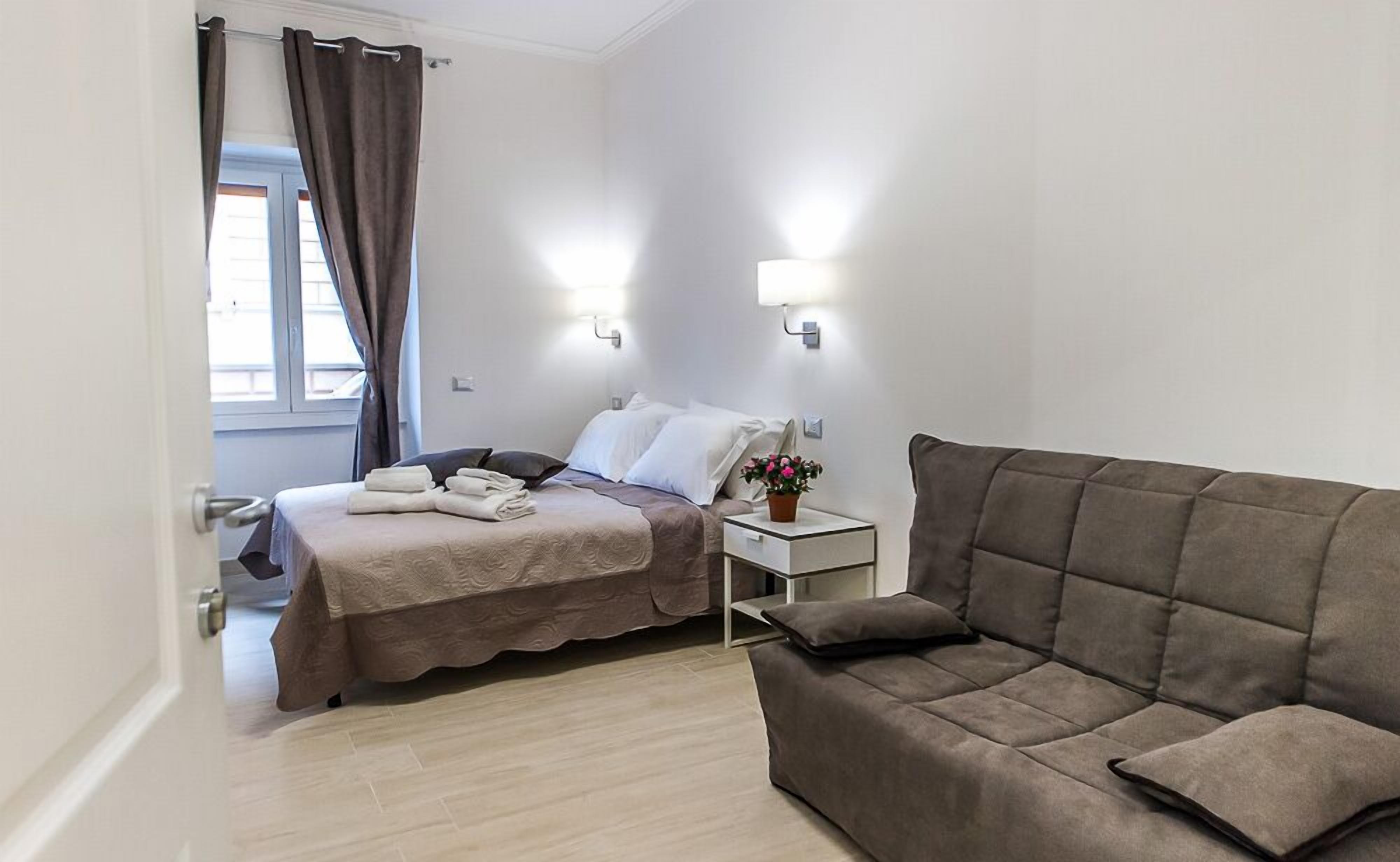 Ein Hotelzimmer mit Bett, Nachttisch, Sofa und einem Fenster mit Vorhängen.