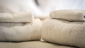 Neatly folded white towels stacked on a bed. - Mr. Charlie Brown (Rome)