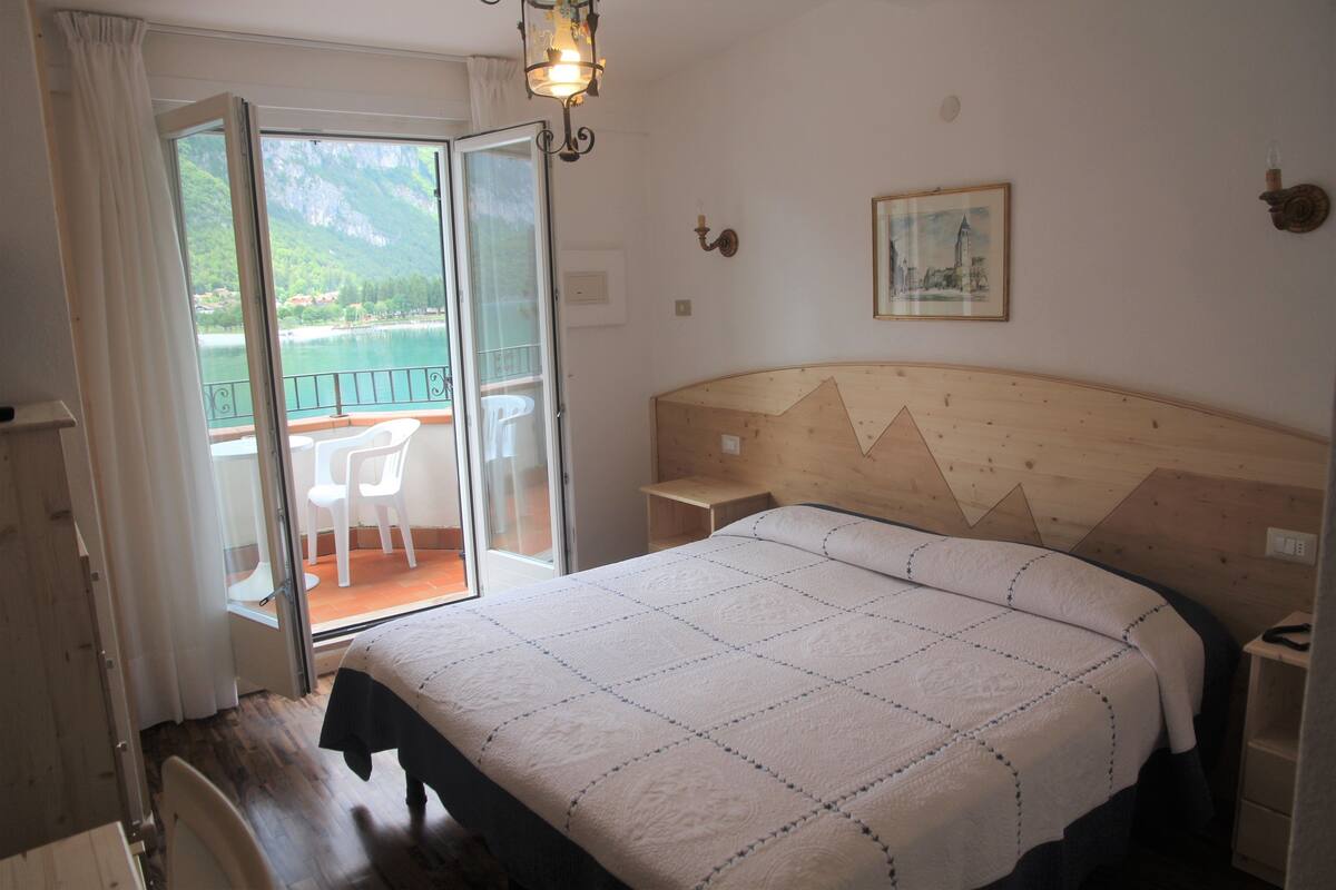 Un dormitorio con una cama grande, cabecera de madera, mesita de noche y vistas a un balcón con sillas.