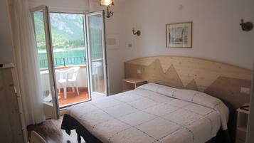 Ein Schlafzimmer mit einem großen Bett, einem hölzernen Kopfteil, einem Nachttisch und Blick auf einen Balkon mit Stühlen.
