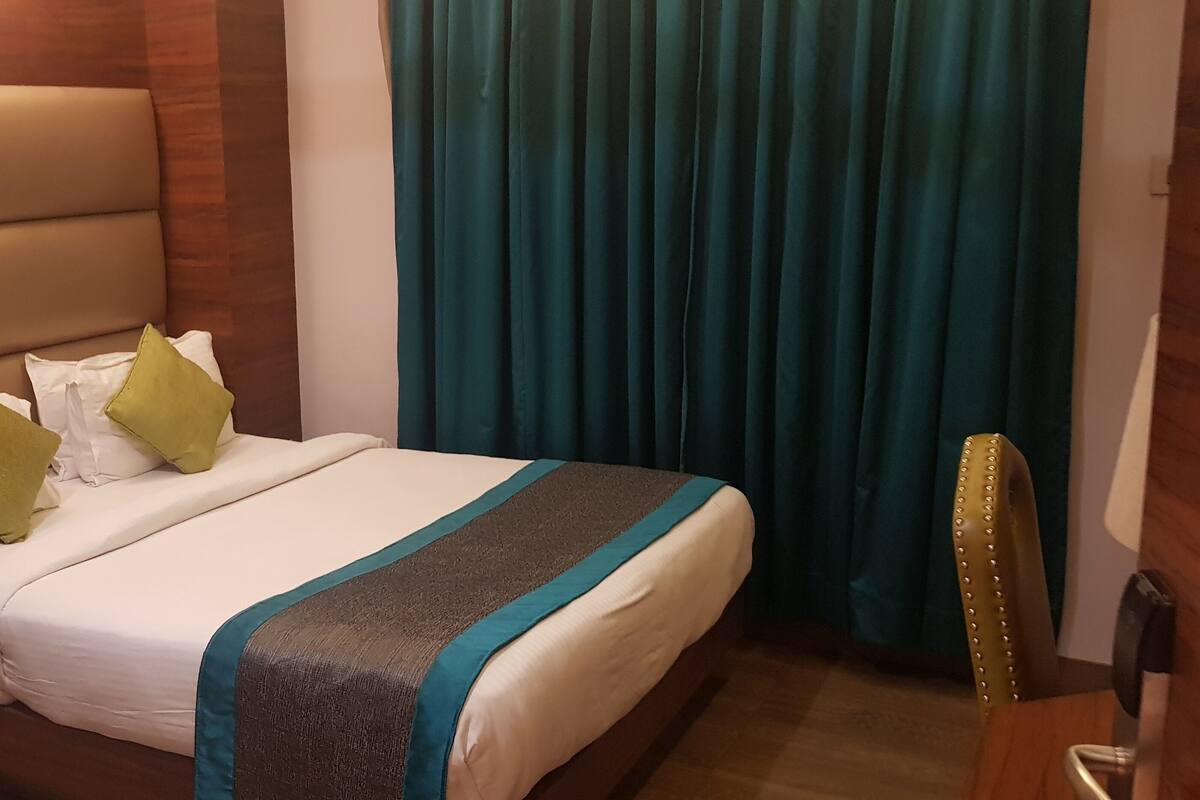 Un lit bien fait, avec des oreillers blancs et verts, une couvre-lit turquoise et grise et une tête de lit en bois.