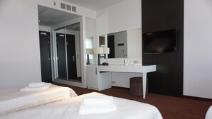 Habitación de hotel con dos camas, un escritorio, un espejo, un televisor y una puerta que da a otra habitación.