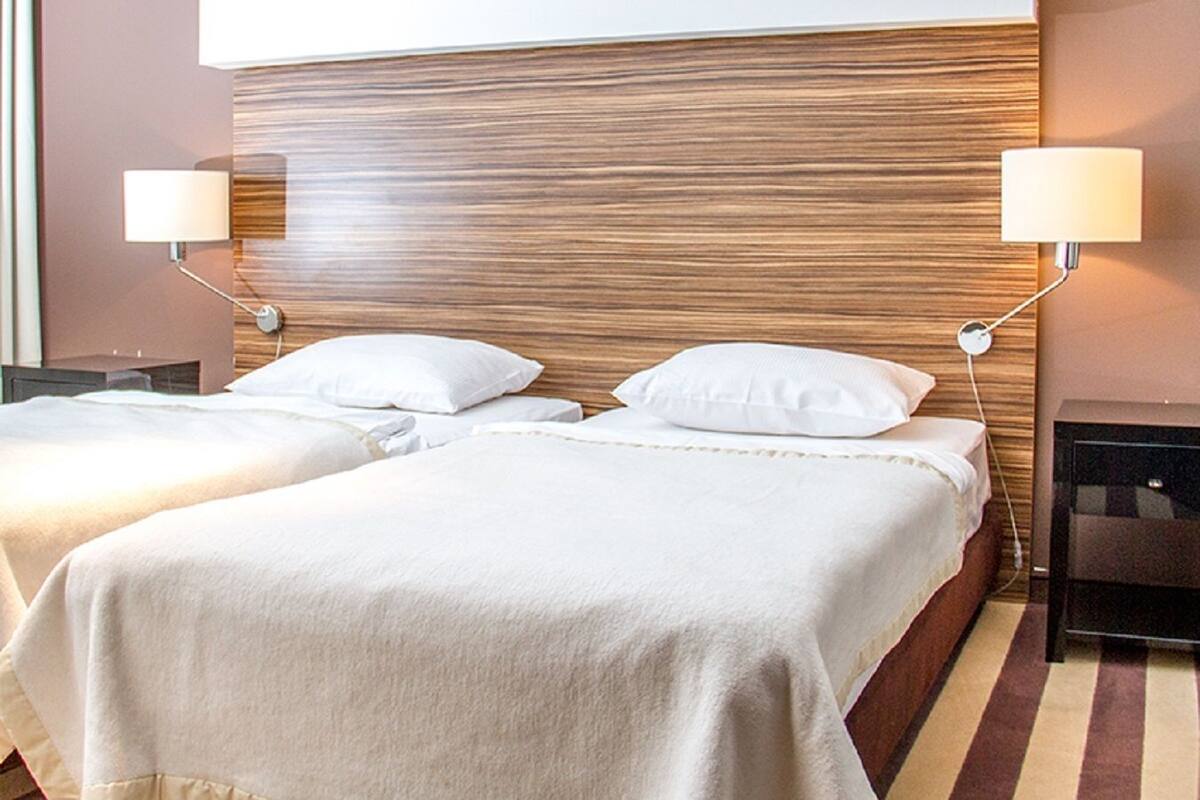 A hotel room with two beds, wooden headboard, bedside lamps, and a striped carpet.