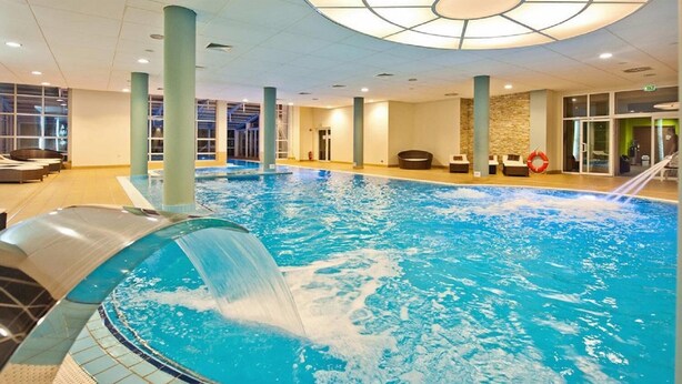 Una piscina interior con tobogán de agua, sillones de descanso y una pared de piedra.