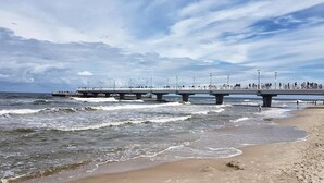 Una playa con un muelle que se adentra en el océano, con un paseo y zonas de estar.