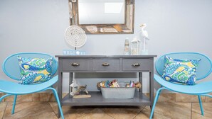 A room with a grey console table, two blue chairs with patterned cushions, a 'WELCOME' sign, a decorative mirror, and a small bird figurine.