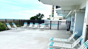 A poolside area with white lounge chairs and a black fence.