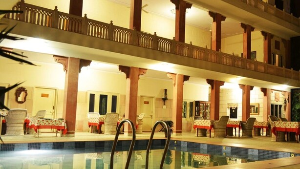 Hotel amb una gran piscina interior, diverses zones de menjador amb taules i caires, i un balcó amb baranes.