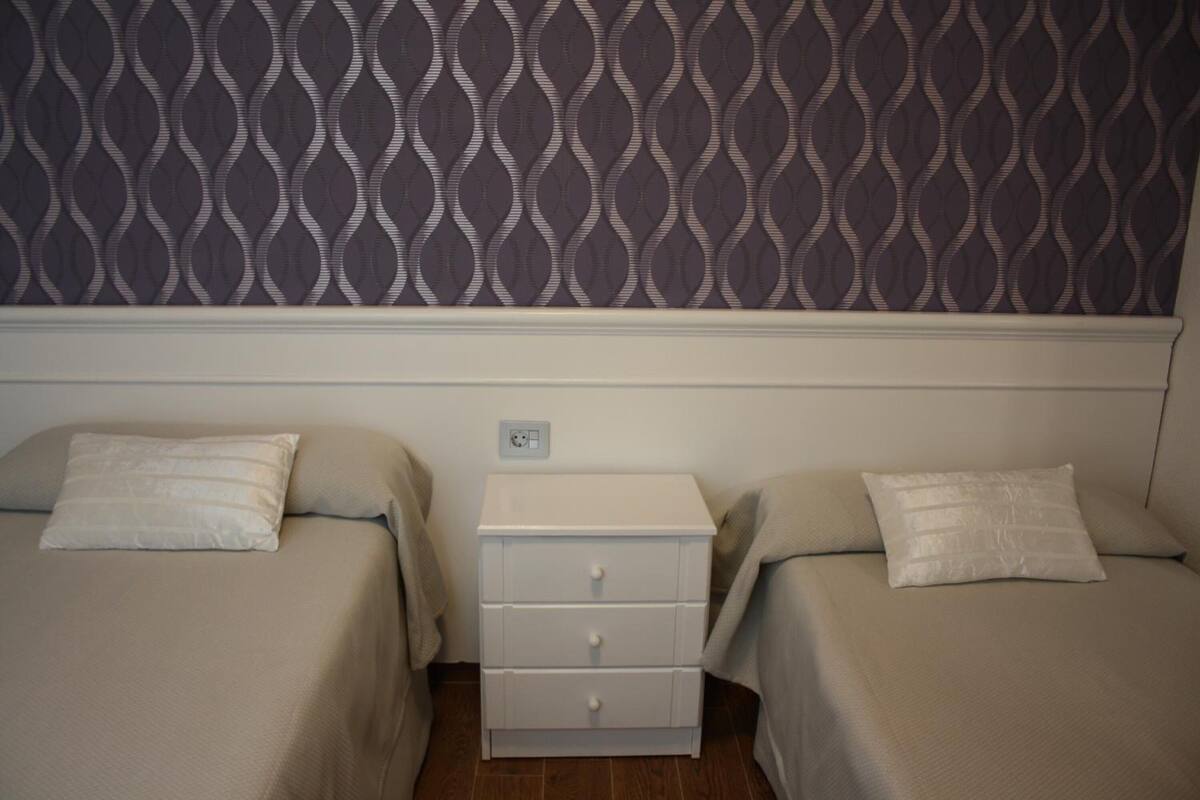 A bedroom with two beds, a nightstand, and a patterned wallpaper.