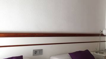 Habitación de hotel con dos camas, una mesita de noche, una lámpara y espejos con forma de sol en la pared.