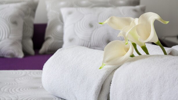 A neatly made bed with white towels and a bouquet of white calla lilies.
