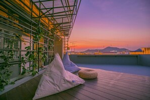 A rooftop terrace with a view of the sunset, a metal railing, and some plants. - Chedi View Hostel & Rooftop Bar (Phetchaburi)