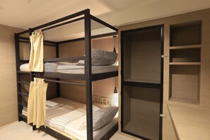 A bunk bed room with a mesh screen door, a small shelf unit, and a plain wall.
