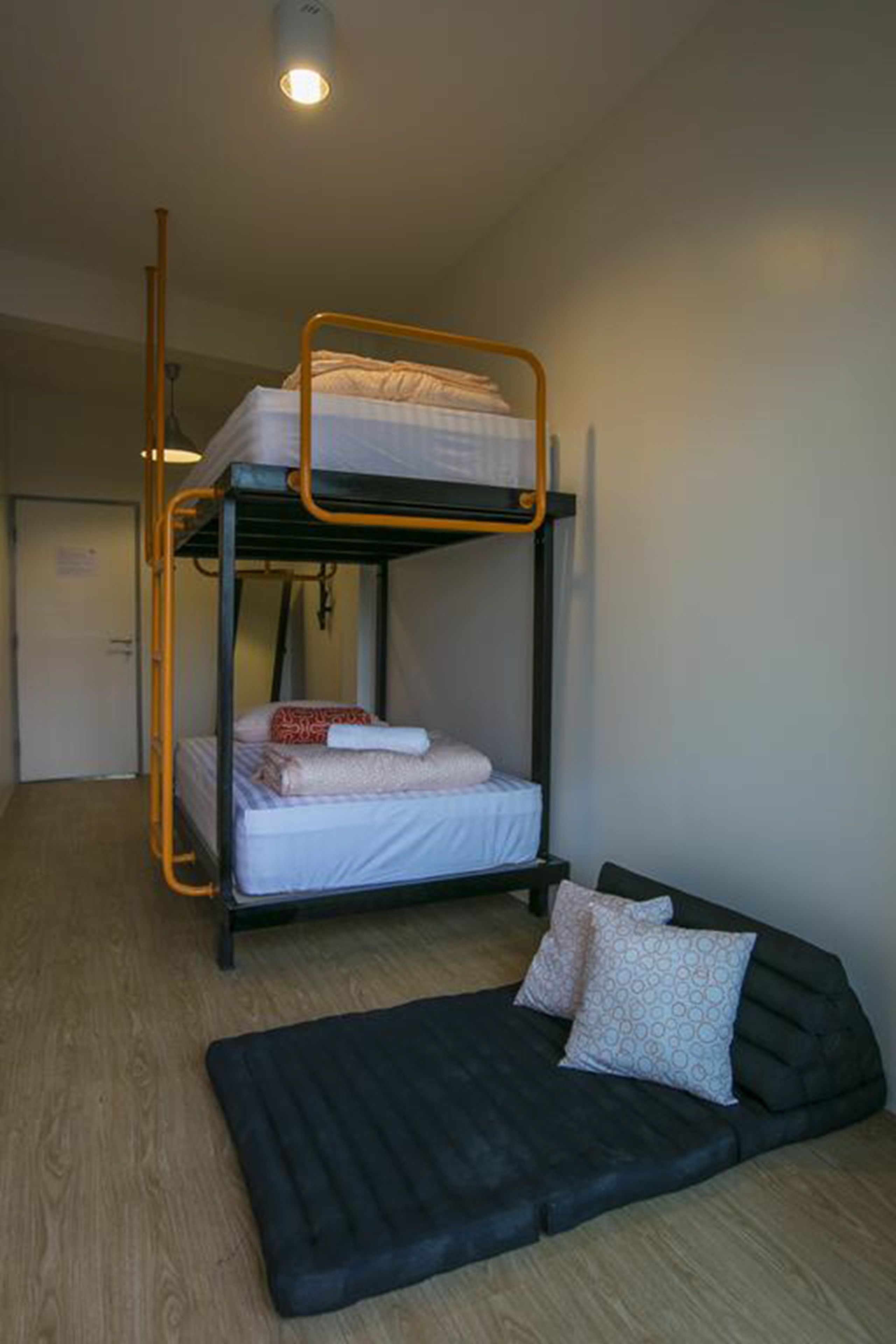 A bunk bed with a mattress and pillows, a sofa with cushions, and a wooden floor.
