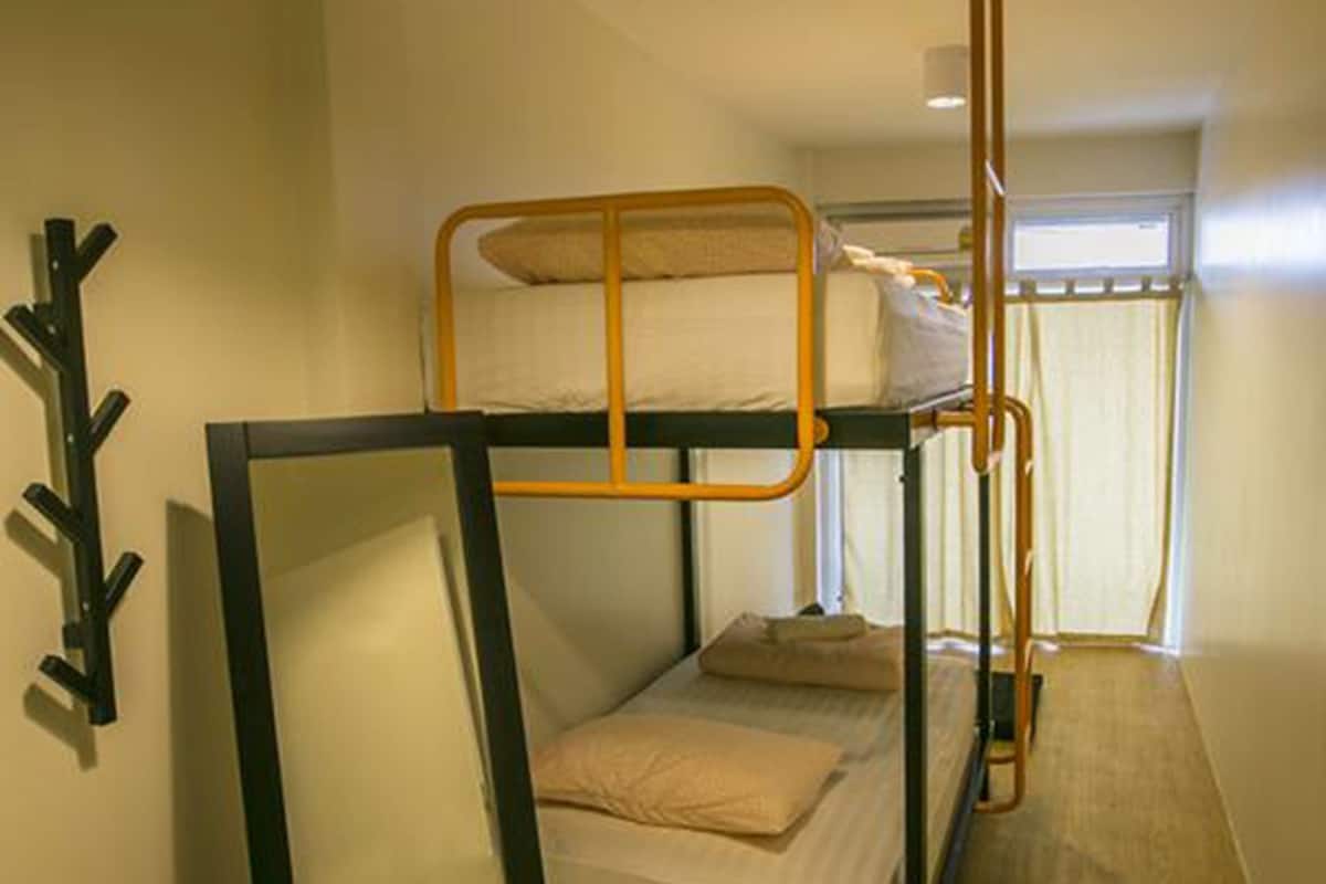 Habitación con literas, una lámpara colgante, perchero y ventana con cortinas.