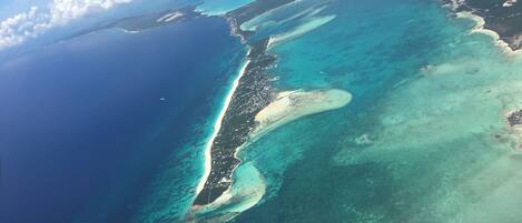 An aerial view of a coastal area with clear blue waters, sandy beaches, and a narrow strip of land with buildings.