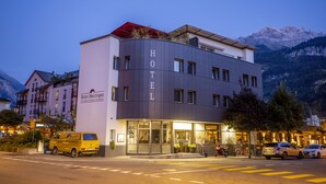 Een hotel met een modern ontwerp, een herkenbare ingang en een berg op de achtergrond.
