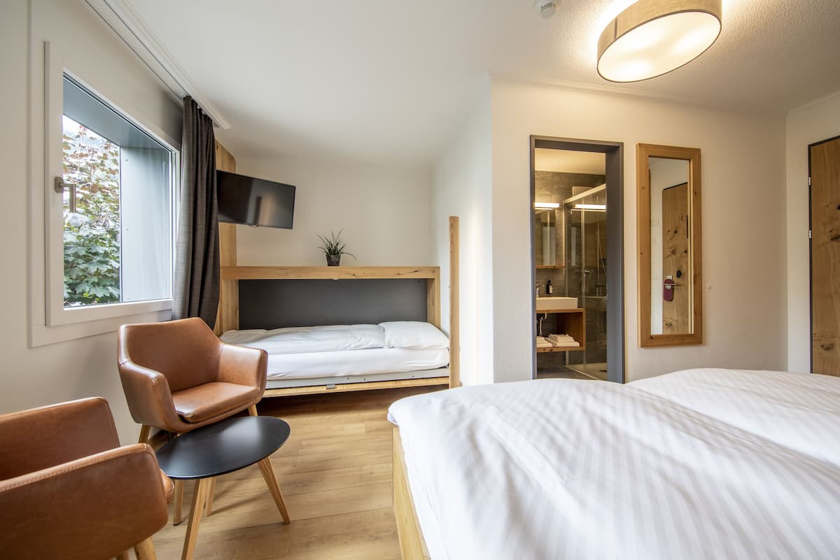 A compact hotel room with a single bed, a small seating area, a TV mounted on the wall, and a window with curtains.
