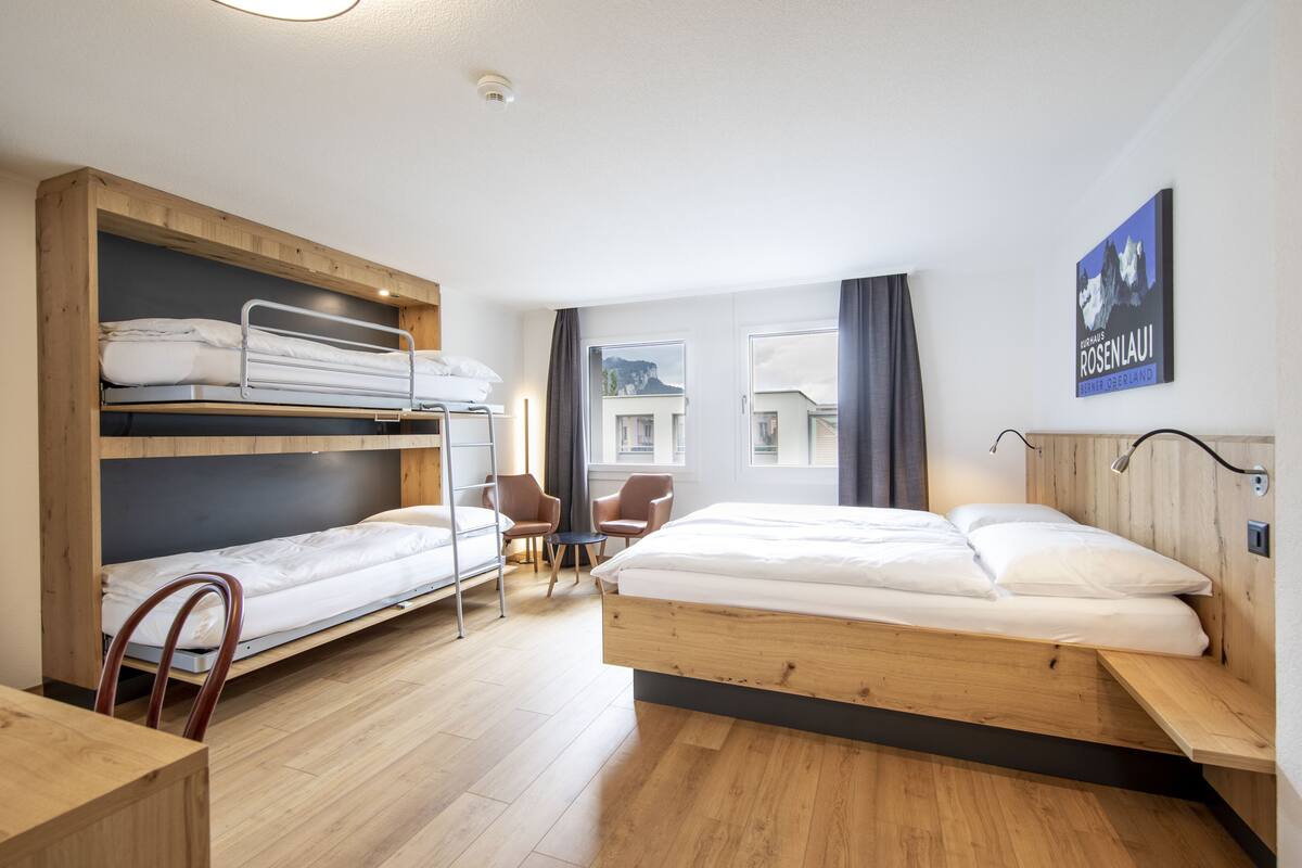 A hotel room with a bunk bed, a desk, two chairs, and a view of a mountain.