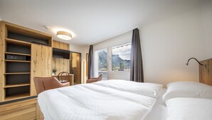 Een hotelkamer met een groot bed, een houten garderobe, een bureau met stoel, en uitzicht op bergen door het raam.