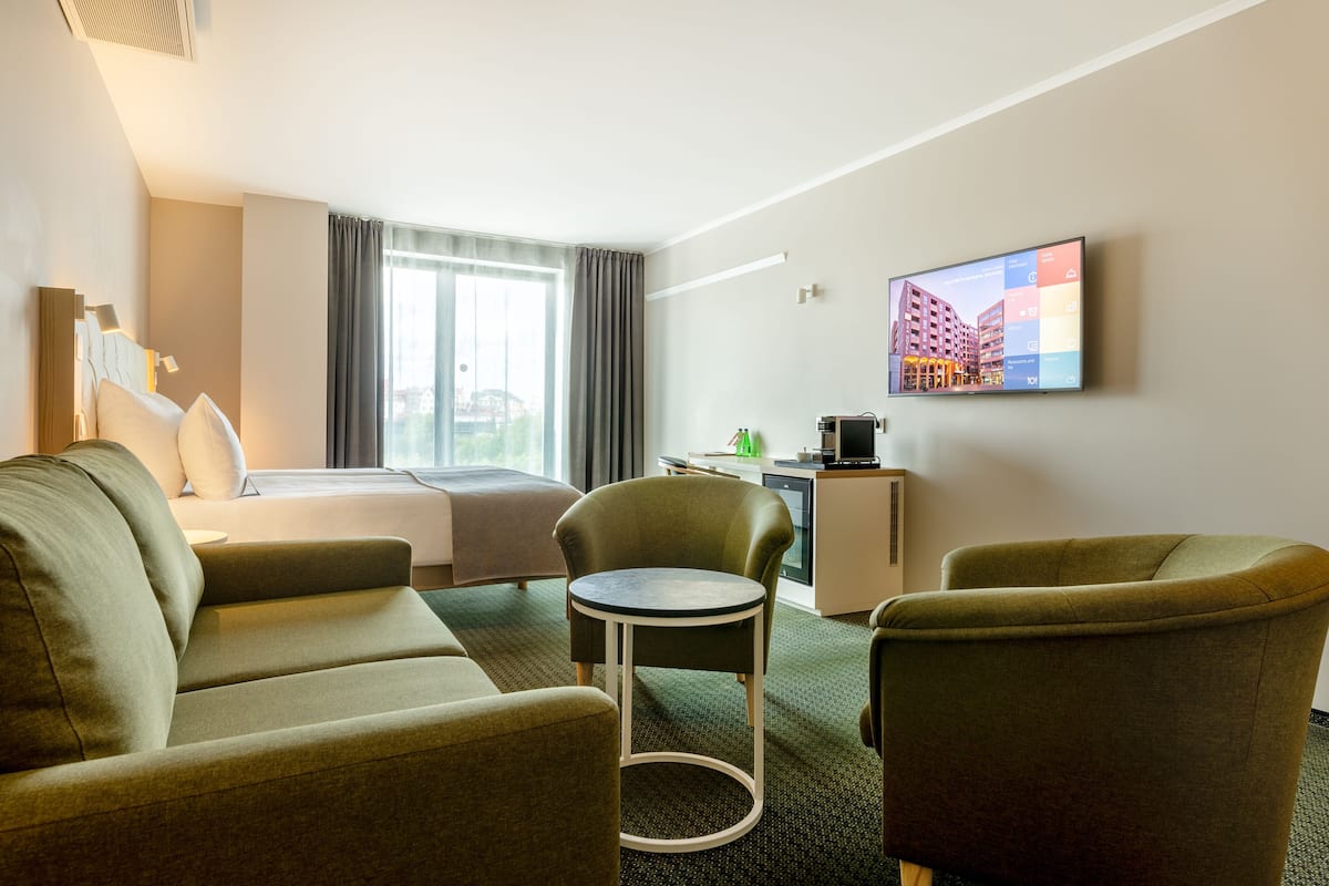Habitación de hotel con cama, dos sillones, una mesita, televisión y ventana con cortinas.