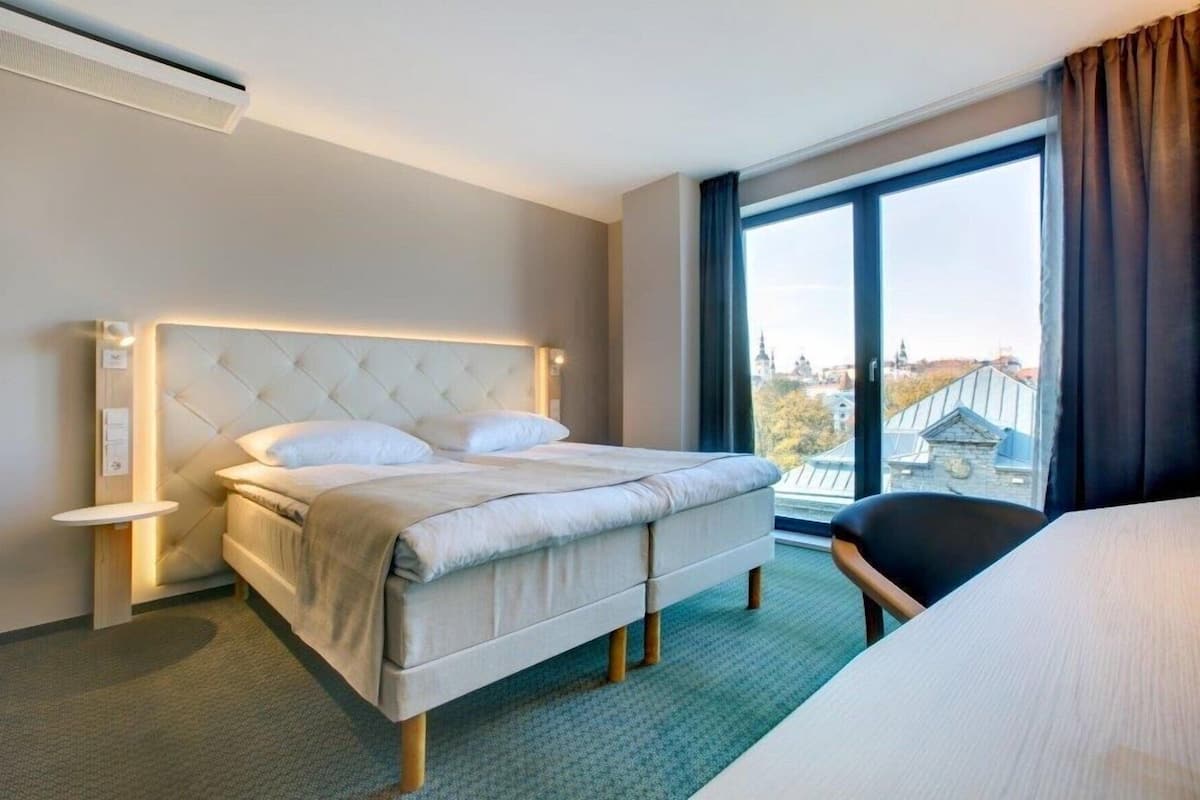 Habitación de hotel con cama, una silla, ventana con vistas y unidad de aire acondicionado.