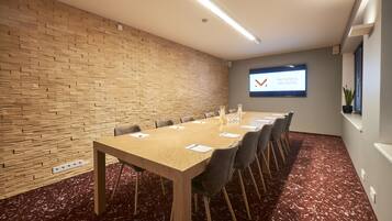A conference room with a long table, chairs, a projector screen, and a brick wall.