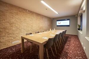 A conference room with a long table, chairs, a projector screen, and a brick wall.