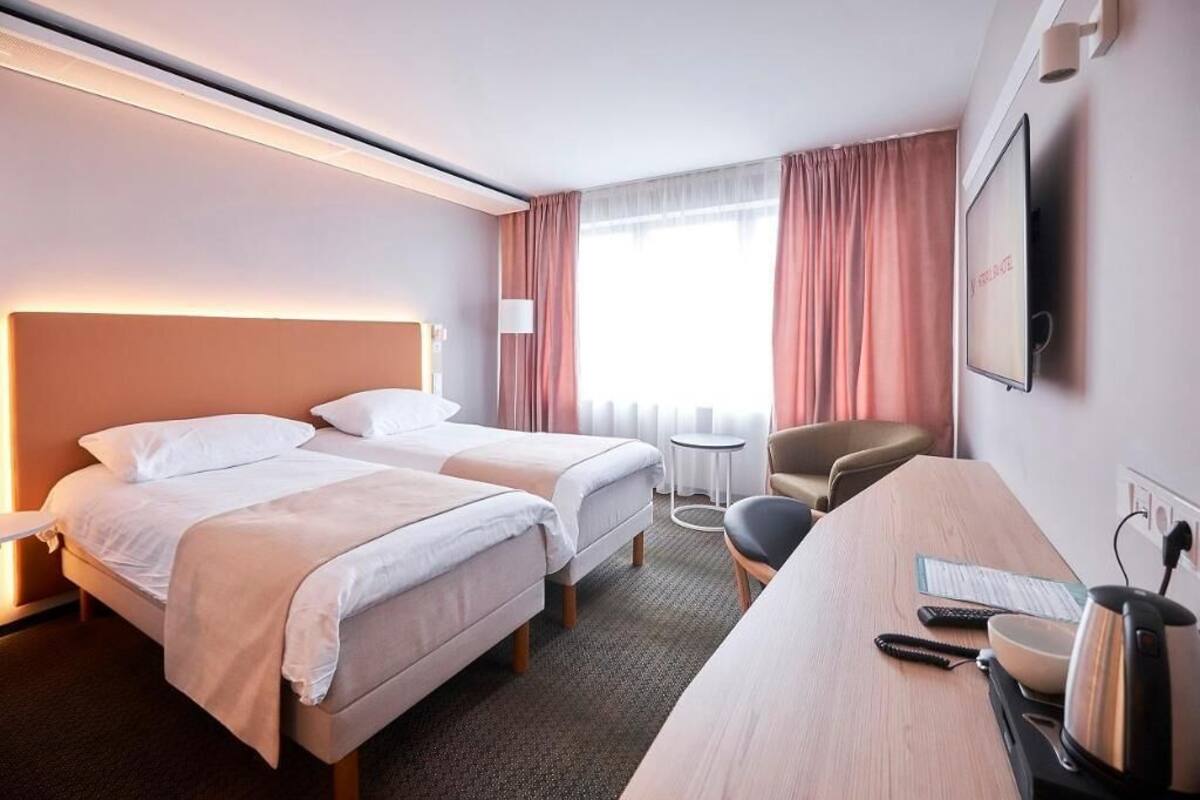 Habitación de hotel con dos camas, un escritorio, una silla, un televisor y una ventana con cortinas.