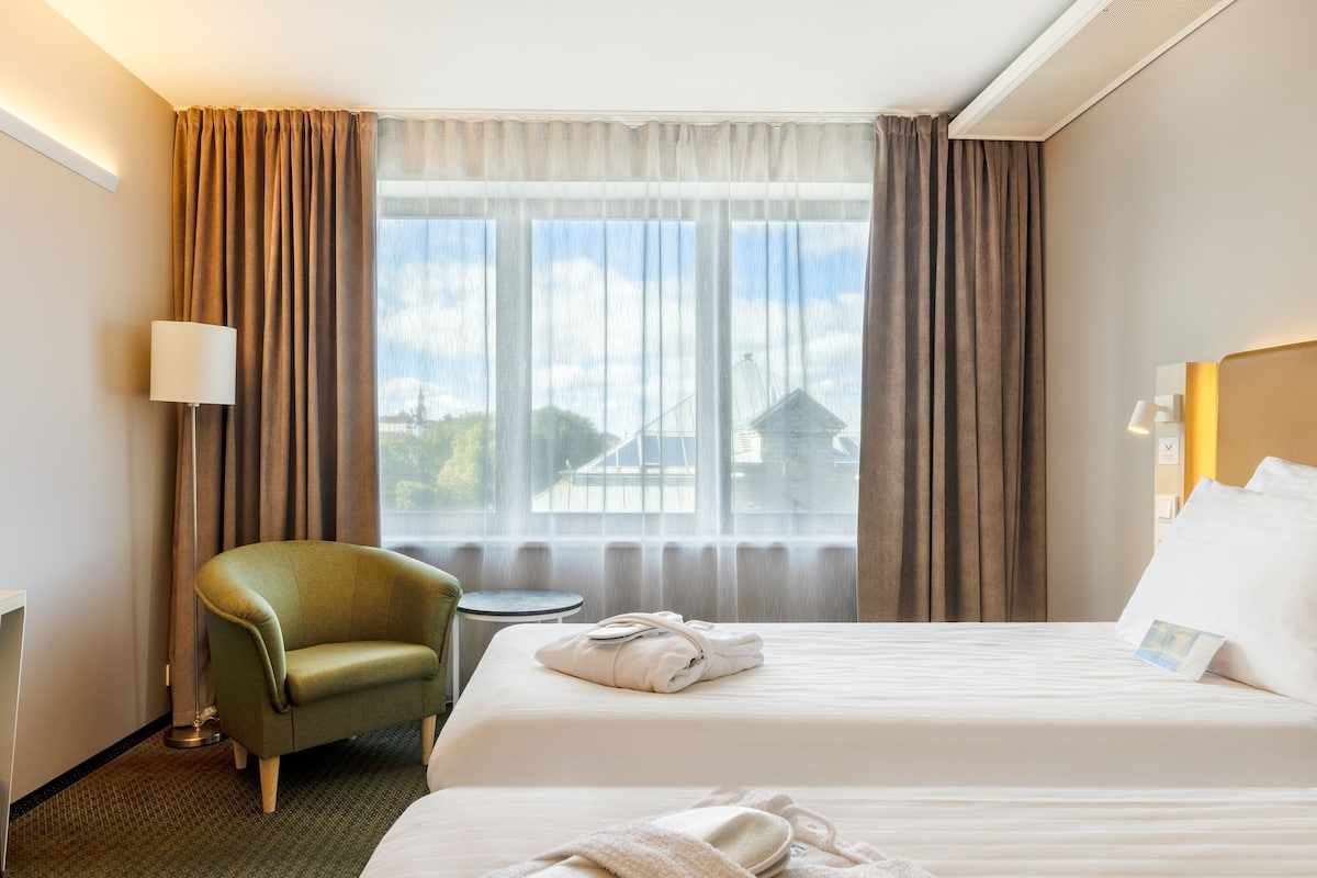 Una habitación de hotel con cama, una silla, una mesita y una ventana con cortinas.