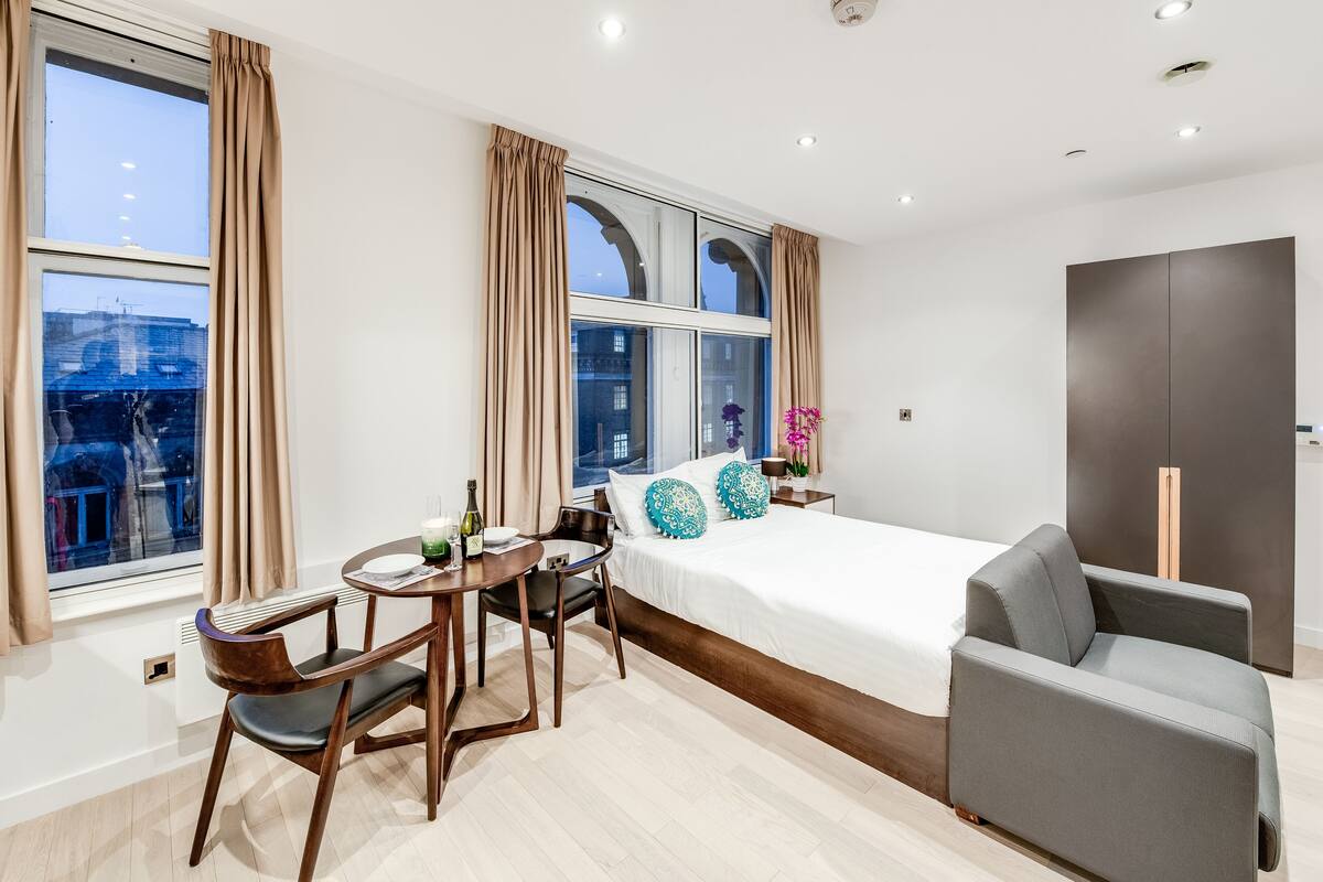 A modern hotel room with a large bed, a desk with a chair, a sofa, and a wardrobe.