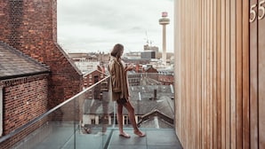 Une personne se tient sur un balcon d’où l’on peut admirer un panorama sur la ville, avec vue sur les immeubles et une tour.