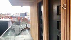 Un bâtiment moderne doté d’une façade en bois, d’un balcon en verre et offrant une vue sur le paysage urbain.