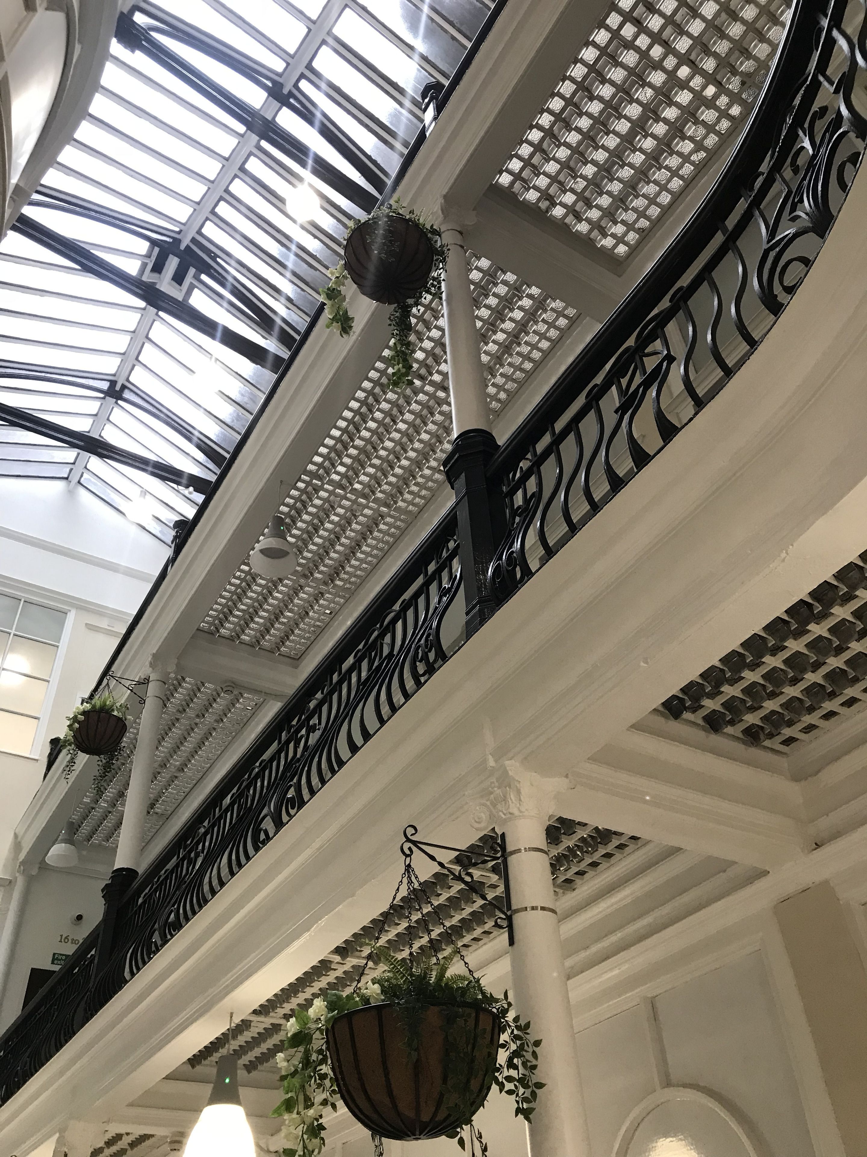 Un atrio ampio con soffitto in vetro, colonne bianche e ringhiere in ferro battuto nero.