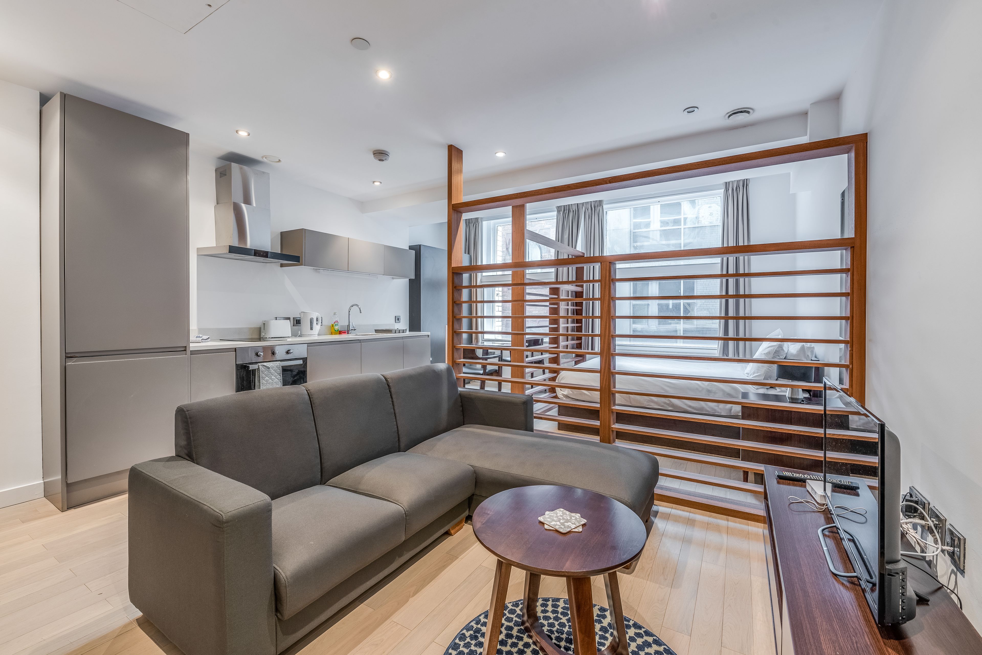 A modern living room with a grey sectional sofa, a small round wooden coffee table, and a TV on a wooden stand.