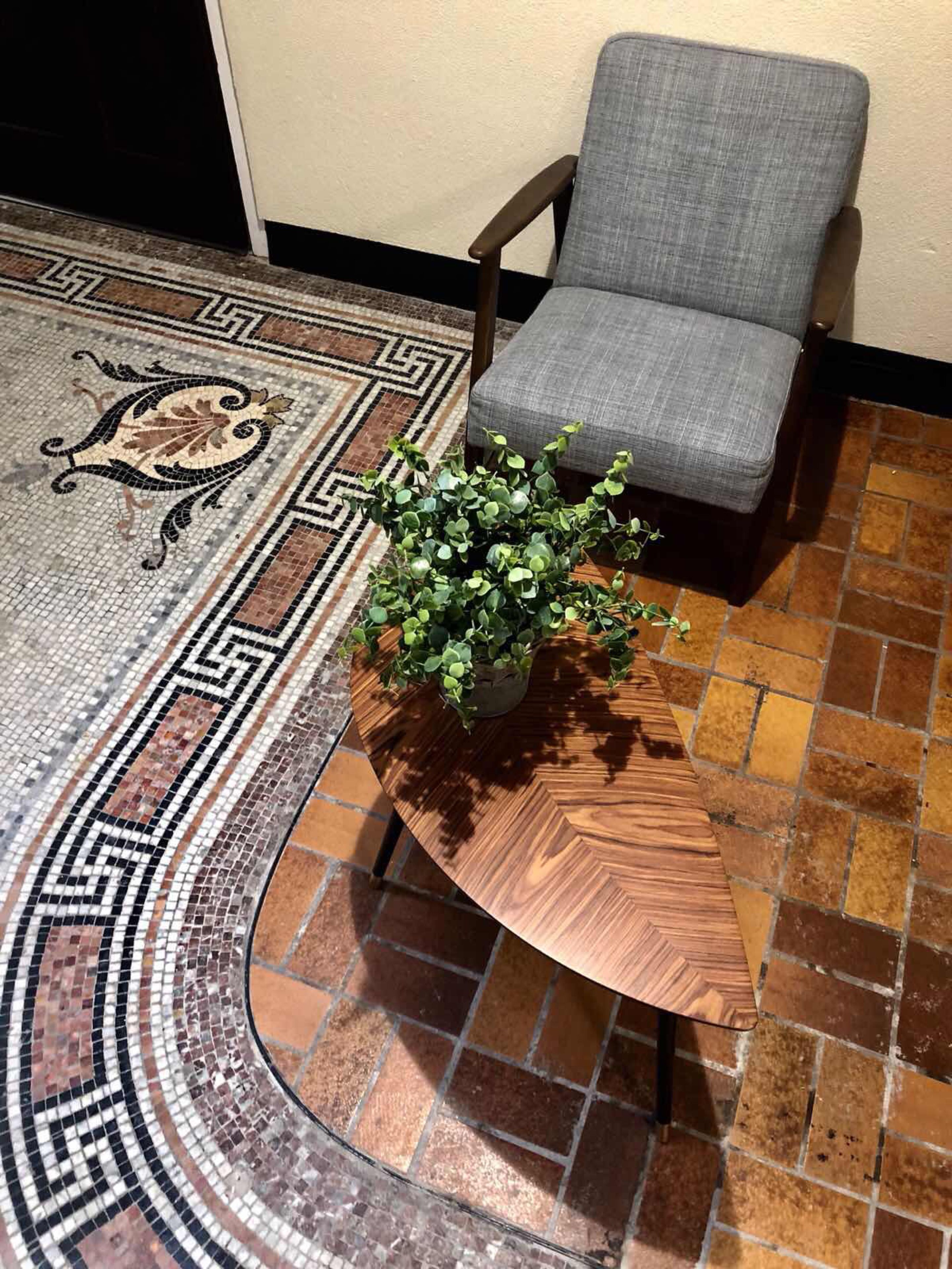 Una stanza con un tavolo rotondo in legno, una sedia imbottita grigia e un pavimento a mosaico.